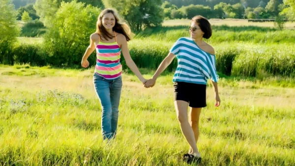 Two women holding hands while walking through a field.