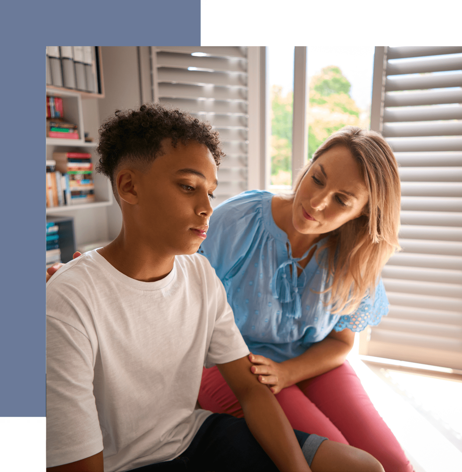 A woman sitting next to a boy in front of window.