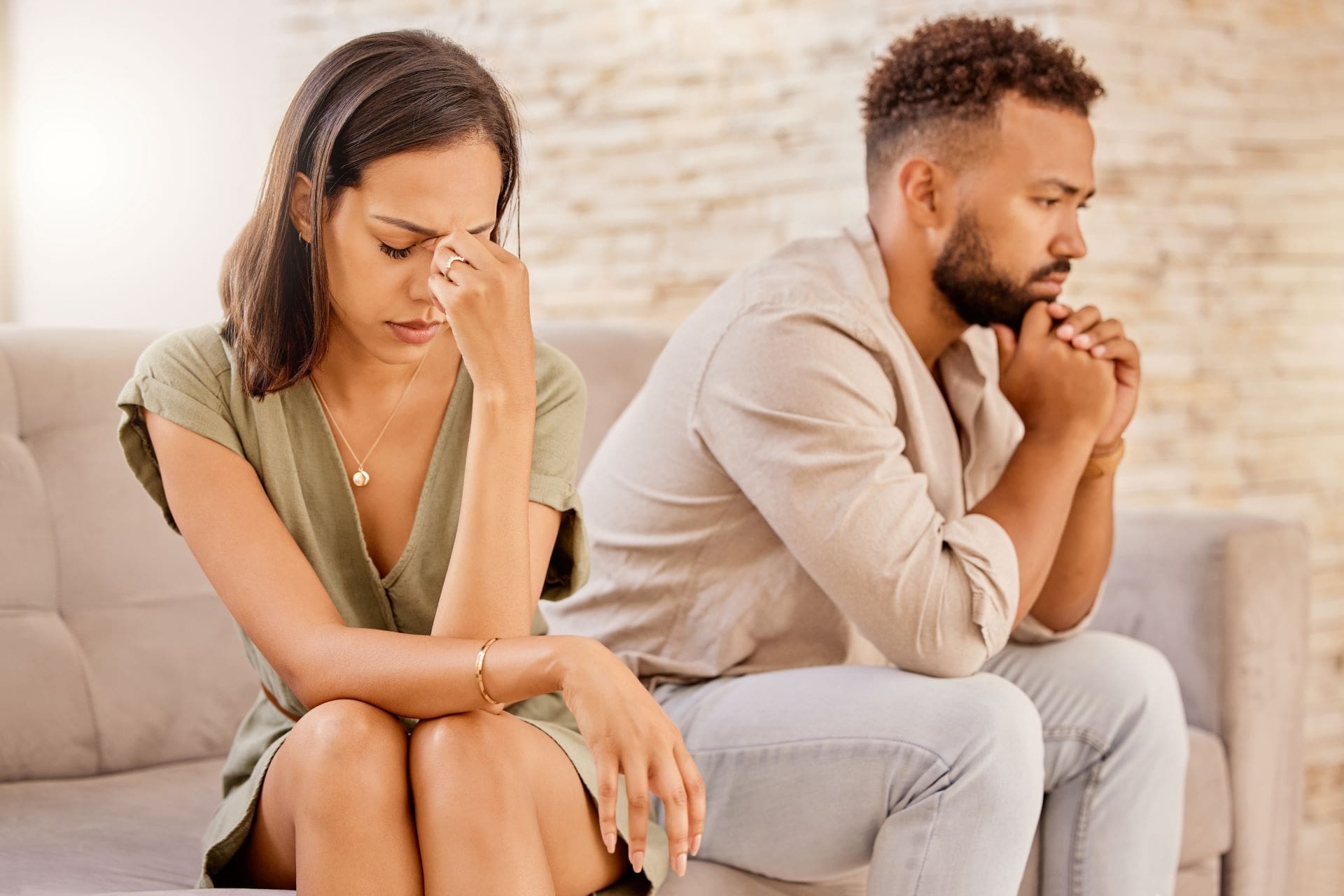 A man and woman sitting on the couch with their hands in their face.