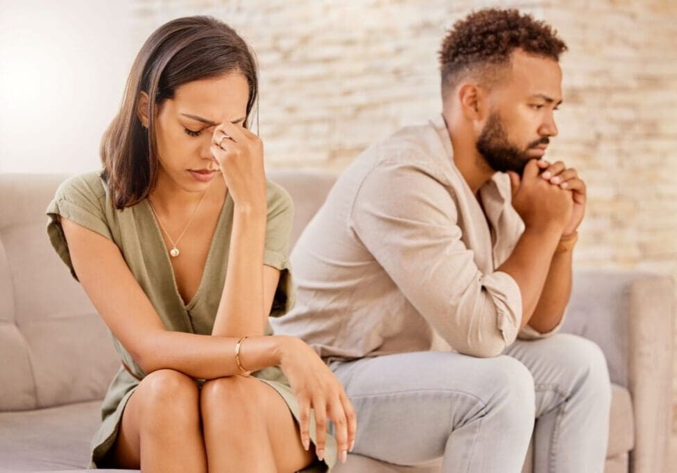 A man and woman sitting on the couch with their hands in their face.